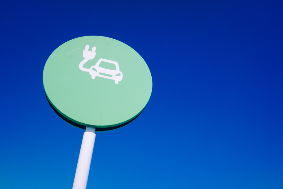 Elektroauto uzlādes simbols uz zaļas zīmes ar zilu debess fonu.
