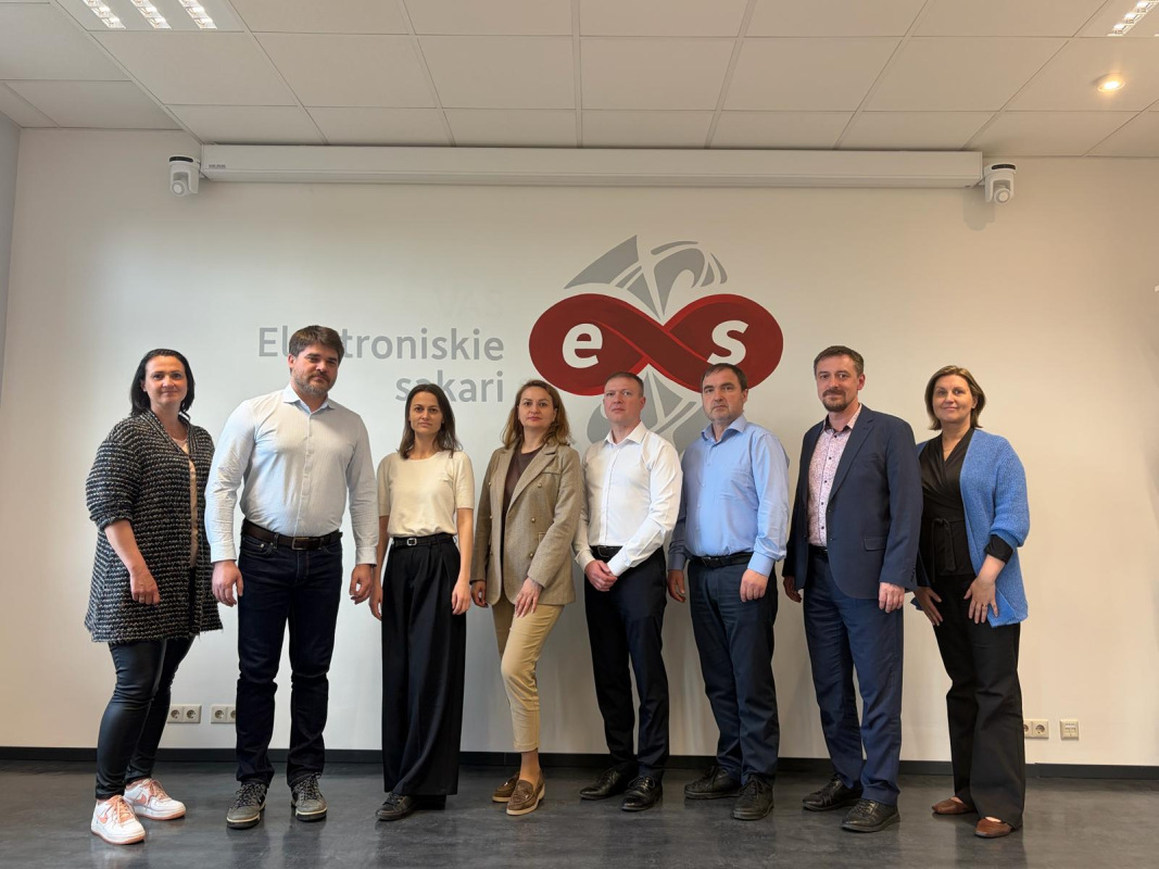 Eight representatives posing in front of the Electronic Communications Office of Latvia logo.