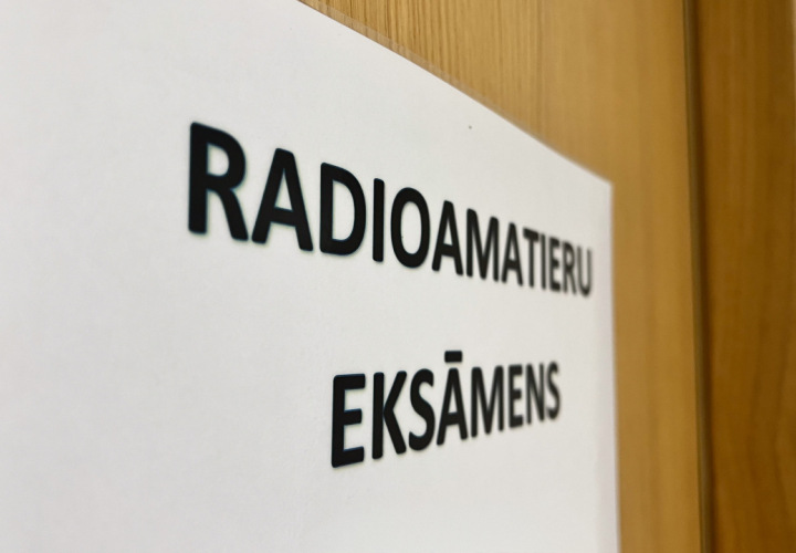 Pie durvīm pielīmēta balta lapa, uz kuras rakstīts ''Radioamatieru eksāmens''