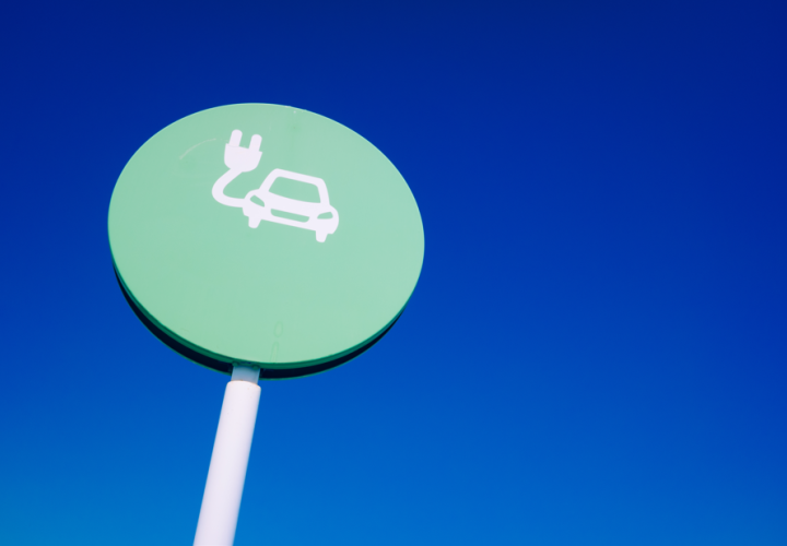 Elektroauto uzlādes simbols uz zaļas zīmes ar zilu debess fonu.