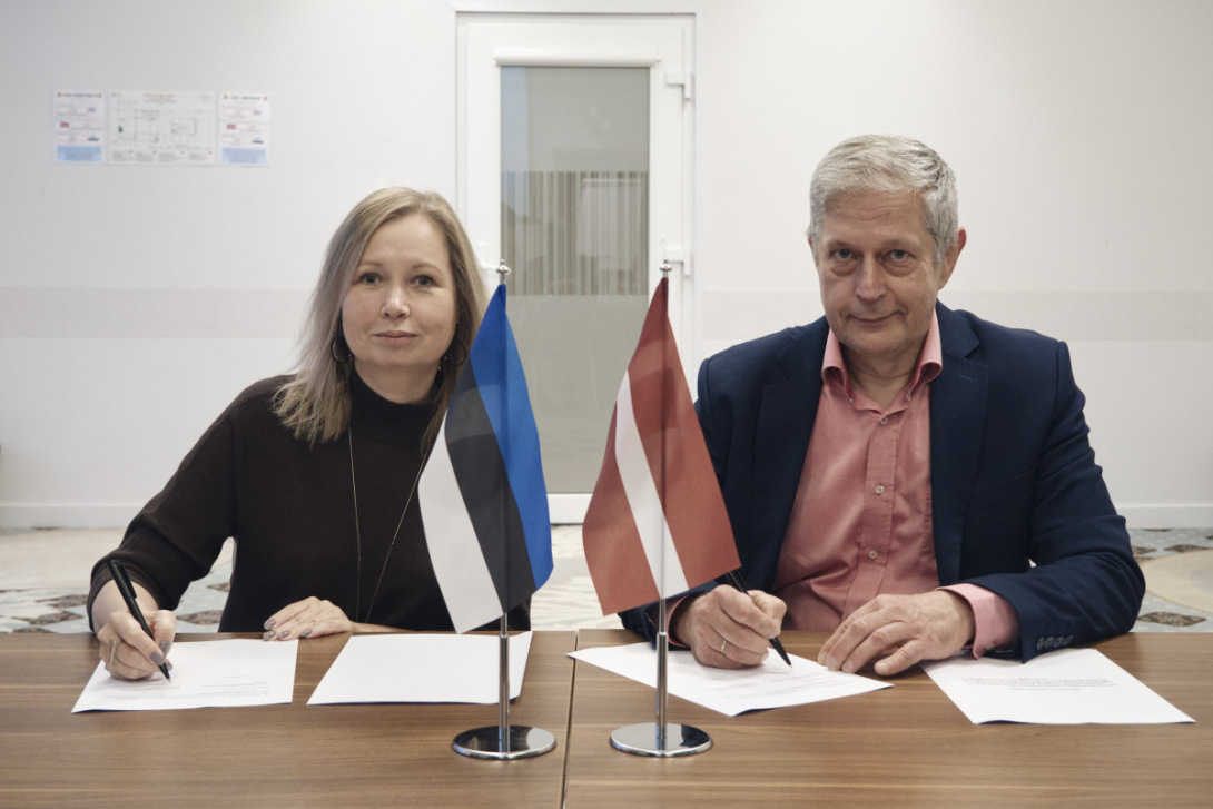 Latvijas un Igaunijas pārstāvji paraksta starpvalstu koordinācijas vienošanos. Uz galda novietoti abu valstu karodziņi.