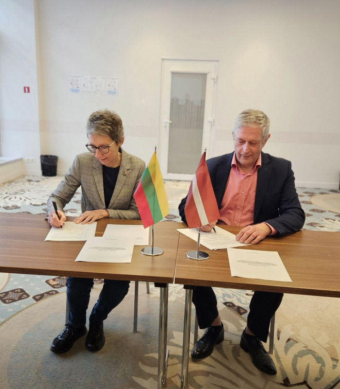 Latvijas un Lietuvas pārstāvji paraksta starpvalstu koordinācijas vienošanos. Uz galda novietoti abu valstu karodziņi.