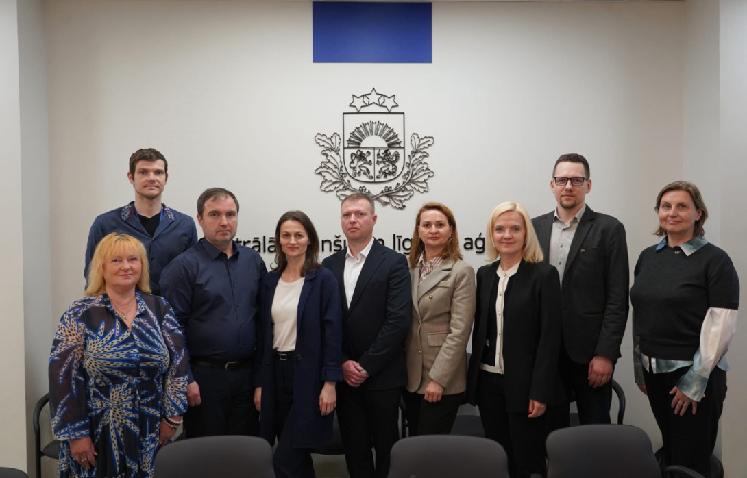 Nine representatives posing in front of the Central Finance and Contracting Agency emblem.