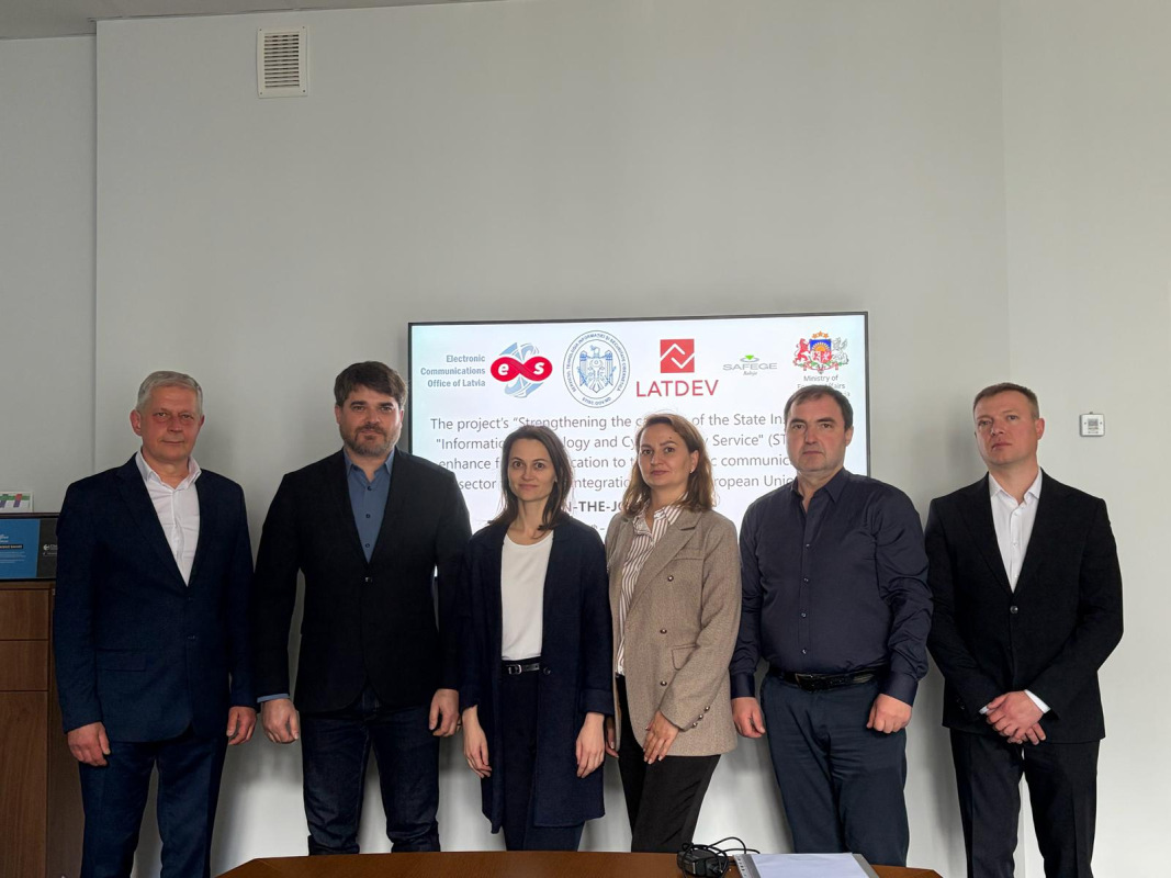 Six representatives posing in front of a presentation screen displaying the project partners’ logos.